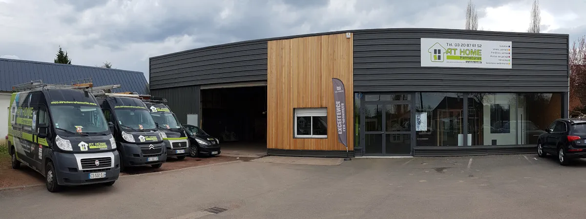 Façade et showroom AT HOME Couvertures & Fermetures à Bailleul, avec véhicules d'intervention