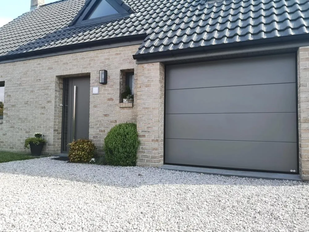 Porte de garage sectionnelle grise et porte d'entrée assortie sur maison en briques